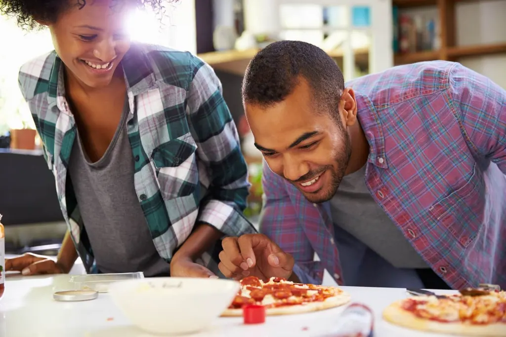 A black couple cooking together in the kitchen making a pizza | men’s issues in san francisco, ca | counseling for men san Francisco | men's therapy san francisco, ca | 94539 | 94110 | 94112